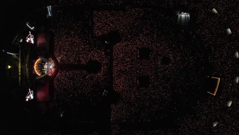 Luftaufnahme-Von-Oben-Nach-Unten-Eines-Konzerts-In-Einem-Großen-Stadion-Mit-Einer-Lichtshow,-Die-Von-Tausenden-Von-Fans-Ausgestrahlt-Wird