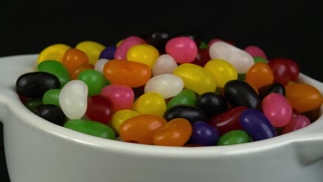 close-up revolving view: colourful jelly beans in white bowl on black