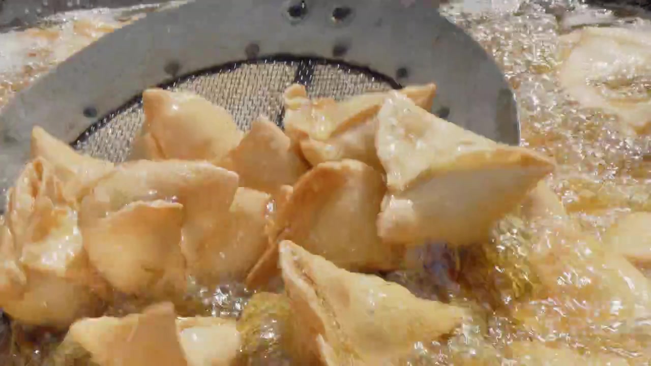 Primo piano al rallentatore: Samosa friggono in olio bollente a un festival all'aperto soleggiato.