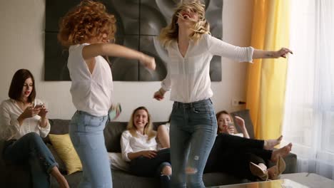 Hen-party.-Group-of-six-attractive-girls-are-having-fun.-Two-girls-are-dancing-in-craziness.-Identical-casual-clothes.-Emotionally-moved.-Indoors.-Slow-motion