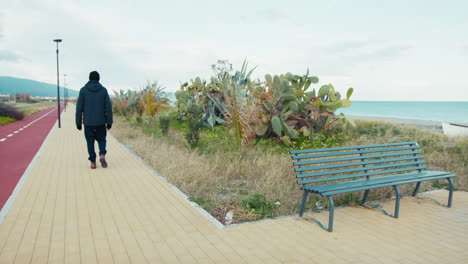 man gets up from the bench near the sea and walks away