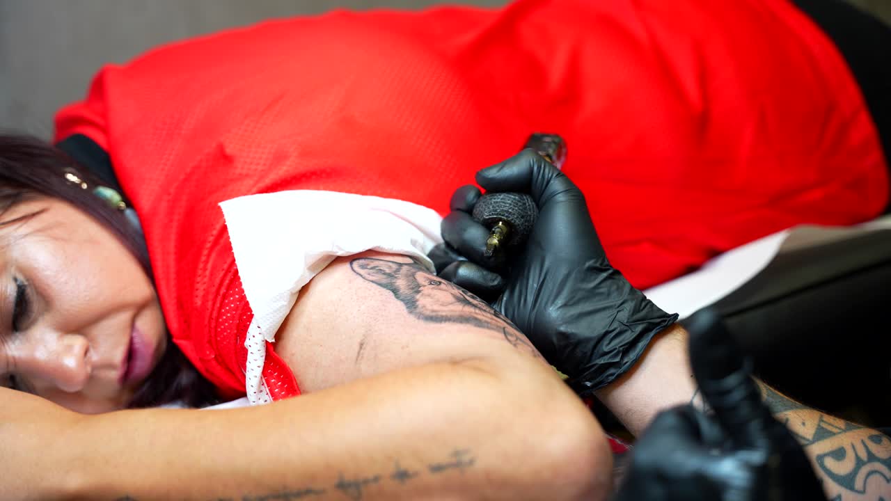 Tattooist doing tattoo art on arm of female client lying on stretcher at studio. Closeup