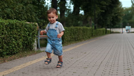 happy smiling caucasian boy is on the walk in the park. kid in jeans romper running outdoors in summer.