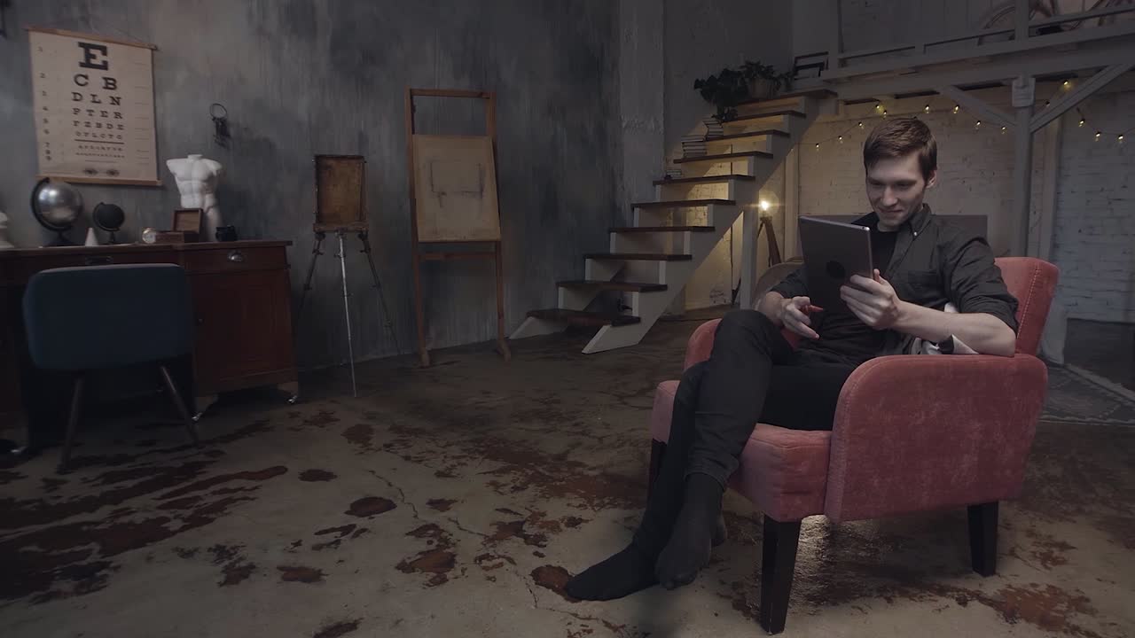человек расслабляется в кресле с планшетом в художественной студии в лофт-стиле
