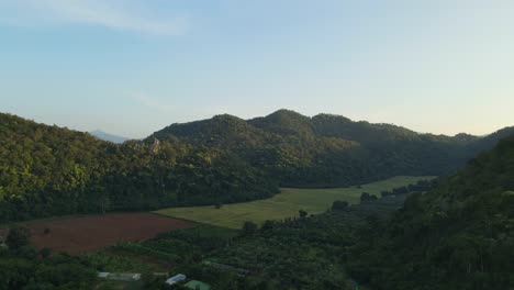 Aerial-footage-sliding-to-the-right-revealing-a-valley-with-farmlands-and-surrounded-by-mountains-in-Pakchong,-Khao-Yai,-Thailand