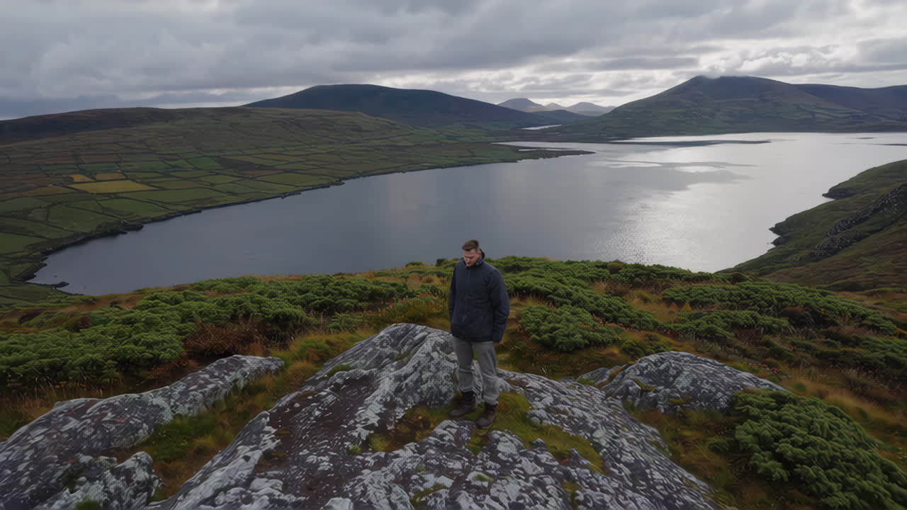 Man on a hilltop overlooking a scenic lake and mountains