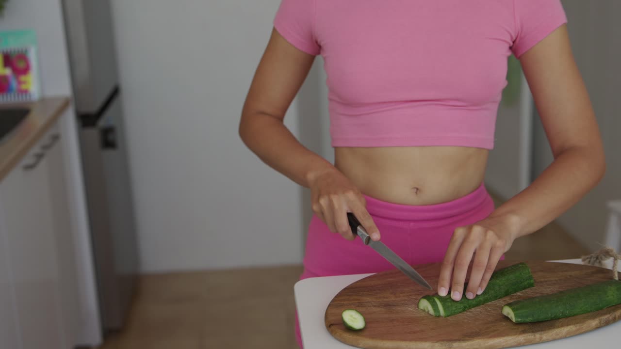 Woman cutting cucumber in kitchen