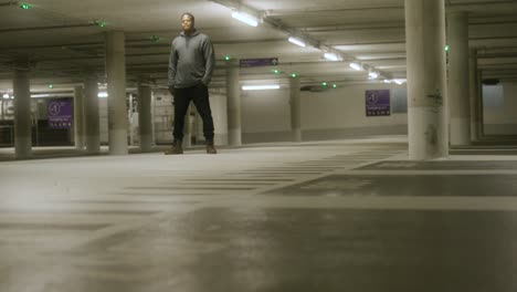 view of cool black male standing with hands in pocket inside empty underground parking lot with bright lights in metzingen, germany, baden wurttemberg, europe, panning view angle