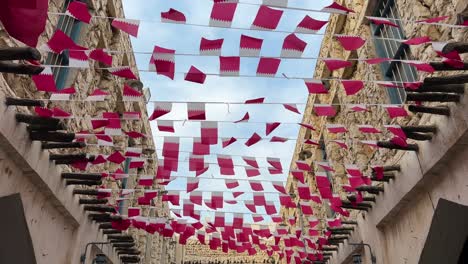 Hölzernes-Designgebäude-In-Der-Alten-Stadt-Doha-Aus-Lehmziegeln-Traditionelle-Häuser-Aus-Adobe-stein,-Entworfen-Von-Farbenfrohen-Katar-flaggentouristen-Mit-Marokko-fanflagge-Am-Tag,-Sonnenscheinwind,-Der-Die-Gastfreundschaft-Der-Ortsansässigen-Winkt
