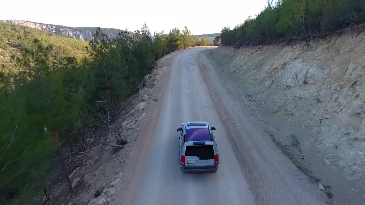 Vista aerea di un SUV che guida su una strada sterrata di montagna remota