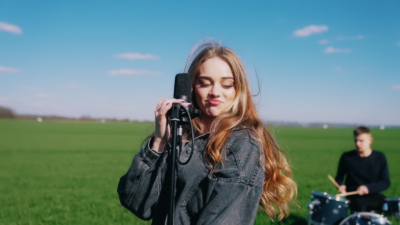 Young woman singer performing music outdoors. Beautiful female soloist singing into a microphone on nature background.
