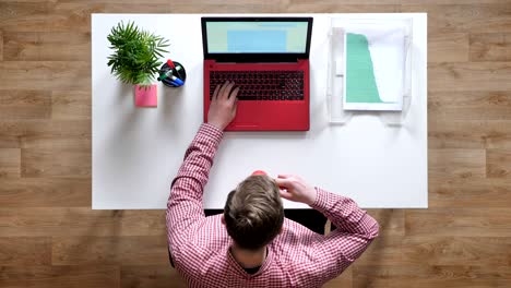 young man in glasses working on laptop and drinking, women giving him coffee, topshot, sitting behind table