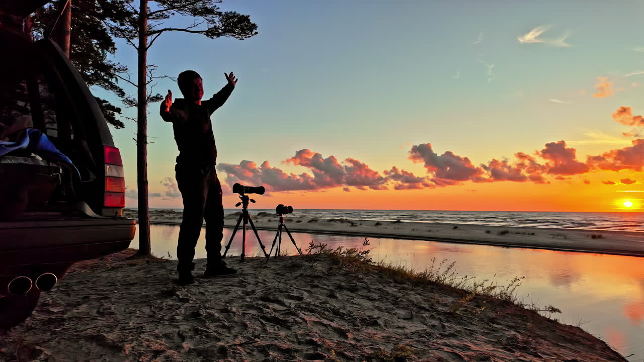 hombre emocionado al lado de un trípode con cámaras instaladas mirando a la impresionante vista de la orilla del océano desde la playa exclamando emoción al atardecer