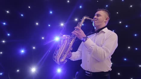 tilt up shot of biracial jazz musician in checkered suit and bowtie playing saxophone while sitting against black band member in dimly lit bar, rehearsing and checking sound before live performance