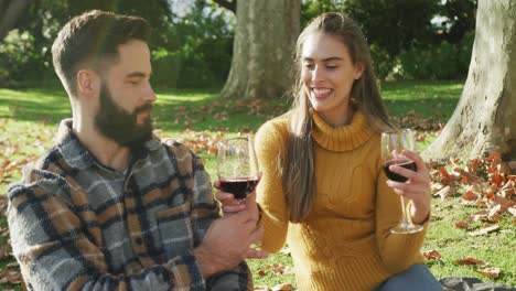 video de una feliz pareja caucásica vestida cálidamente bebiendo vino en el jardín