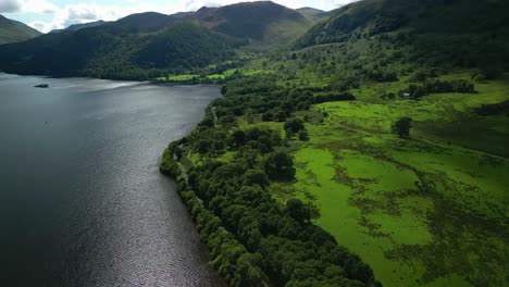 Dark-sparkling-lake-surrounded-by-mountains-with-lush-green-countryside-and-lakeside-road-A592-with-traffic-on-bright-summer-day