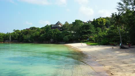 Tranquil-exotic-beach-with-white-sand-washed-by-calm-clear-water-of-turquoise-lagoon-in-front-of-luxurious-resort-in-ko-pha-ngan,-Thailand