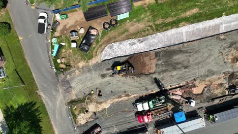 excavator backs up and removes dirt with bucket as it compacts ground in construction site