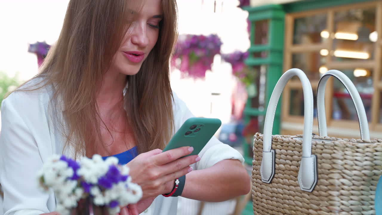 Woman texting at a a table with flowers on it at an outdoor cafe