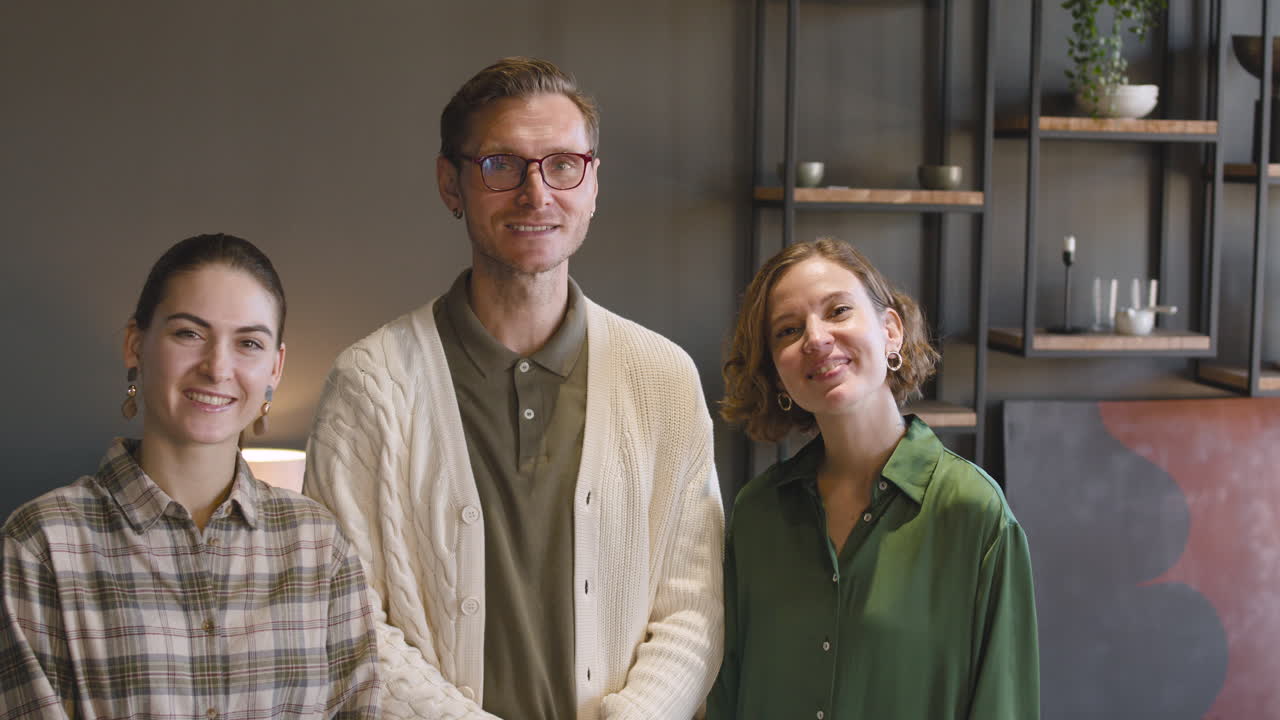 группа из трех человек улыбается и машет в камеру, стоя в современной гостиной дома