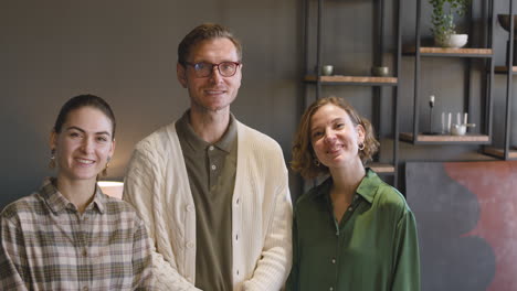 group of three people smiling and waving at camera while standing in a modern living room at home