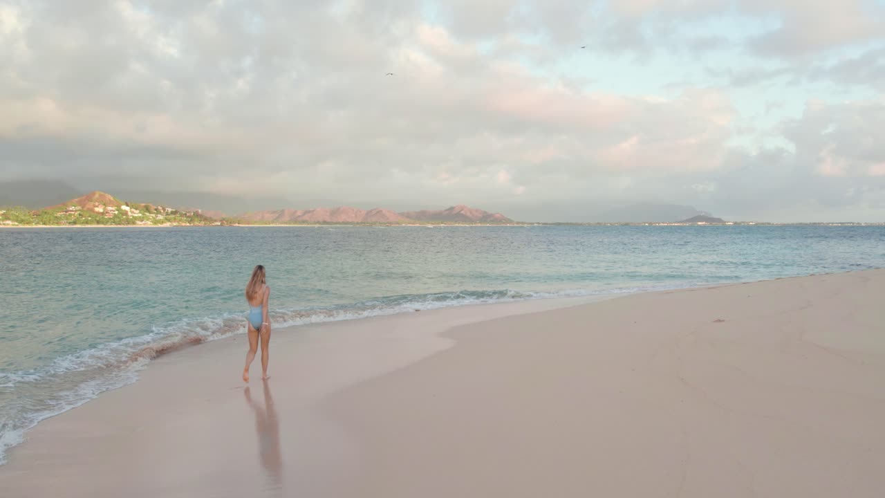황혼에 열대 해변을 걷고 있는 수영복을 입은 젊은 여성, 슬로우 모션