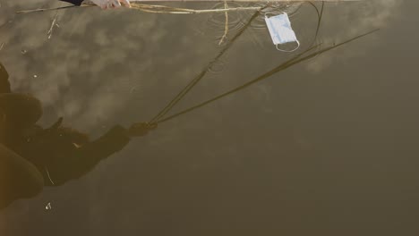 anonymous person pulling out medical mask from lake