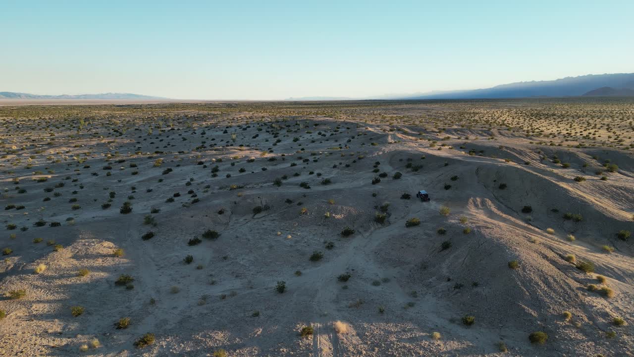 Un veicolo fuoristrada side-by-side scala lentamente una bassa collina nel Messico settentrionale mentre il drone si alza, rivelando un paesaggio arido e deserto illuminato lateralmente dalla luce dell'ora d'oro