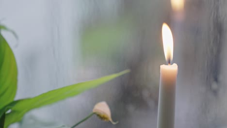 Brennende-Kerze-Und-Eine-Friedenslilie-An-Einem-Fenster-An-Einem-Regnerischen-Tag