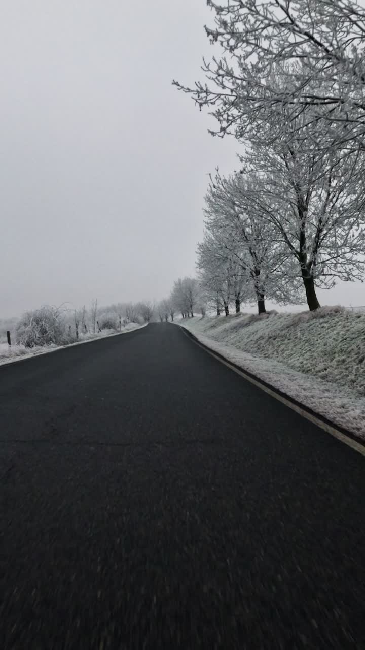 POV from a car riding the open road with trees in snowy winter, overcast