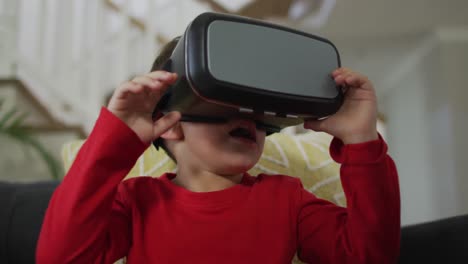 Caucasian-boy-wearing-vr-headset,-sitting-on-sofa-and-having-fun