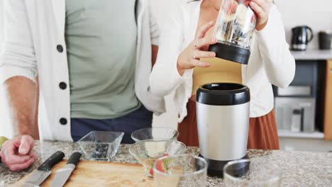 midsection of caucasian couple preparing heathy smoothies in kitchen, slow motion