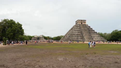 tourists visiting temple of kukulcan (el castillo), dominates the center of the chichen itza archaeological site.temple of the warriors in the background.