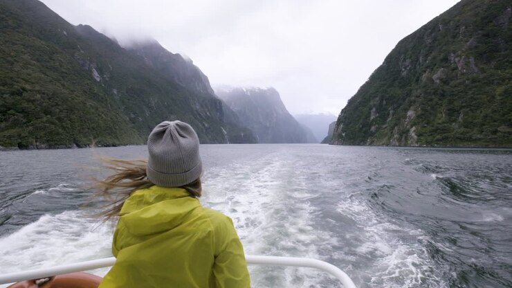 Zeitlupenaufnahme eines Mädchens in gelber Regenjacke auf dem Heck eines Bootes, umgeben von Bergen und Fjorden