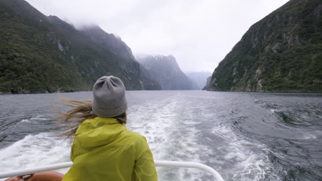 slow motion shot of girl in yellow rain jacket on back of boat surrounded by mountains and fiords