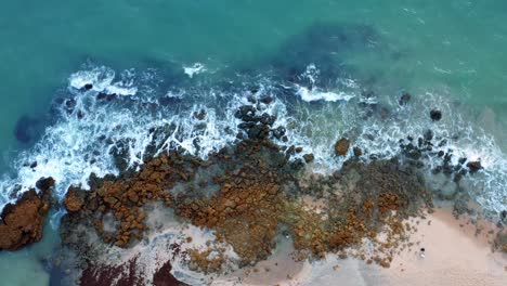 Wunderschöner-Blick-Aus-Der-Vogelperspektive-Auf-Meereswellen,-Die-An-Einem-Warmen-Sommertag-Auf-Felsen-Am-Ufer-Eines-Tropischen-Strandes-Im-Norden-Brasiliens-Namens-Tabatinga-Mit-Blauem-Wasser-Und-Goldenem-Sand-In-Der-Nähe-Von-Joao-Pessoa-Treffen