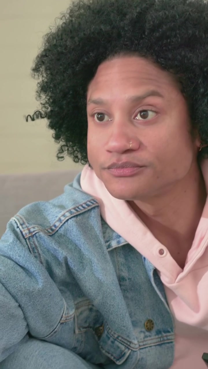 Vertical video: Turning, man in denim jacket pink hoodie taking red bottle on home sofa, copy space