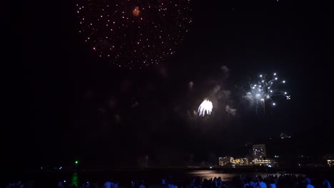 siluetas de multitudes de personas viendo muchos fuegos artificiales explotando sobre la ciudad del océano en japón