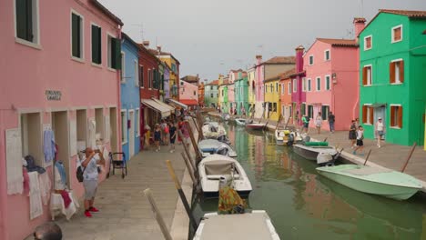burano, venice, italy - tourists wandering along the canals lined with boats and bright, colorful houses - pan right shot
