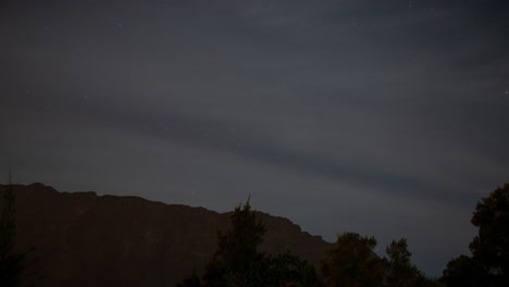 lapso de tiempo de estrellas y nubes moviéndose más allá de una montaña y árboles en primer plano 4k