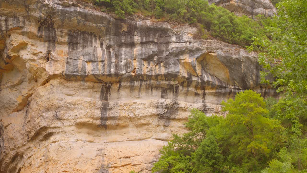View of the dramatic limestone cliff at Grotte du Mas d’Azil in Ariège, France, surrounded by green vegetation