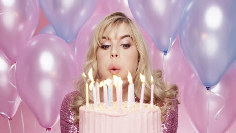 beautiful young woman blowing out candles celebrating birthday pink and blue balloon background - red epic dragon