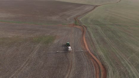 Disparo-De-Drones-Panorámico-Hacia-Abajo-Mirando-El-Tractor-Agrícola-Conduciendo-A-Través-De-Un-Campo-Montañoso