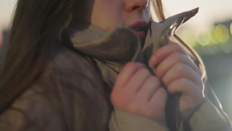 close-up of a girl in a peach jacket, clutching it tightly as she feels cold in a chilly atmosphere. her expression and body language convey the discomfort and need for warmth in a brisk environment