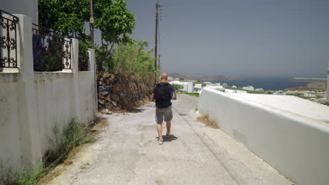 following a man walking down a narrow street of a greek island-1