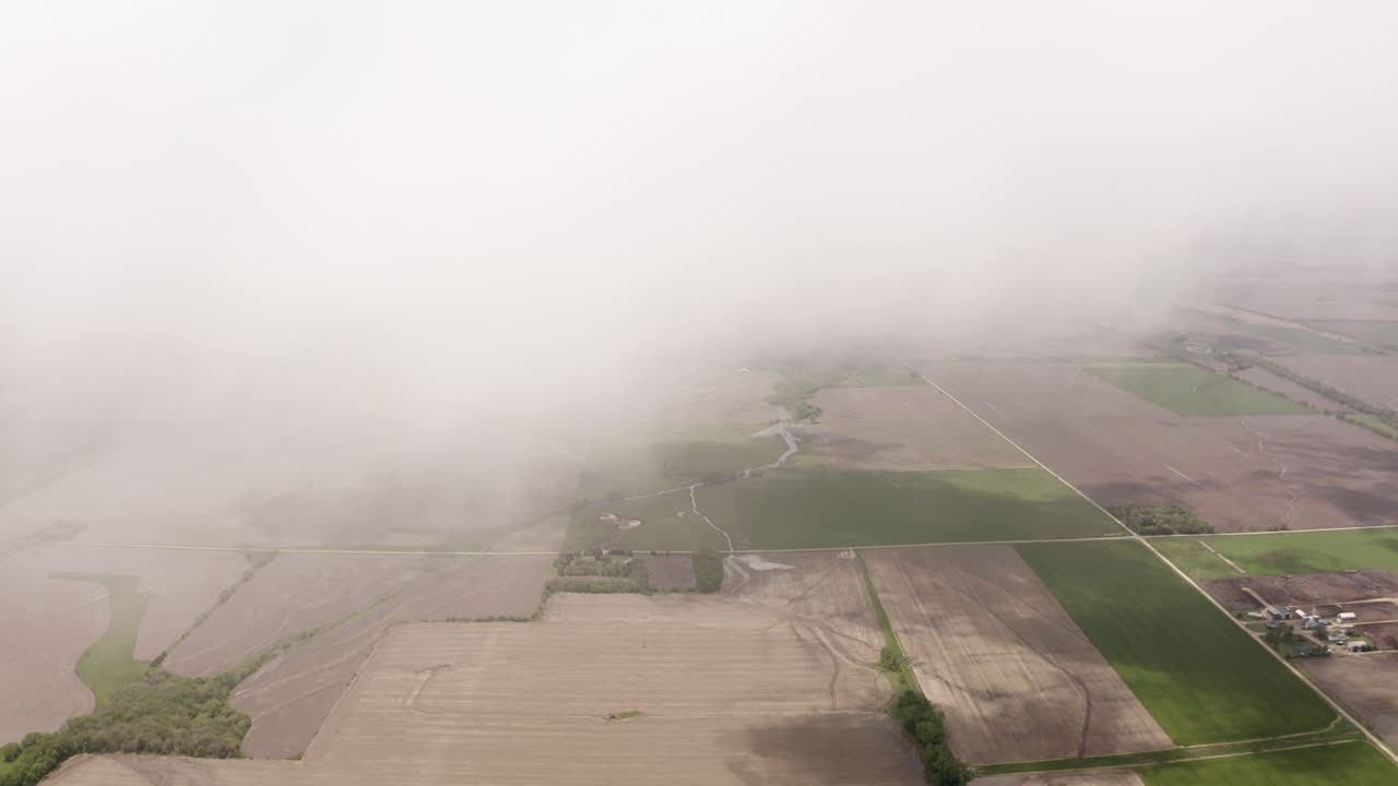Aerial drone moves through clouds above grassland and farmland in midwest of United States