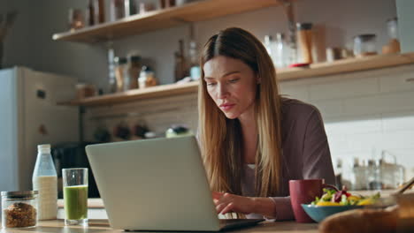 smiling housewife chatting laptop at kitchen close up. woman freelancer typing