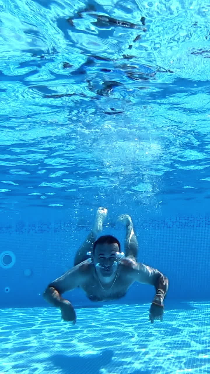 Handsome man diving into the water of the pool. Man swimming underwater in the clear water of the swimming pool. Healthy lifestyle. Vertical video