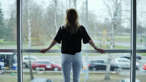 back view of woman in casual clothes gazing through modern window at riga street
