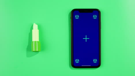 phone with green screen chroma key on green background close up, top view with green lipstick near. summer bright texture studio shot for travel business, delivery, food, cosmetology, make up, application.